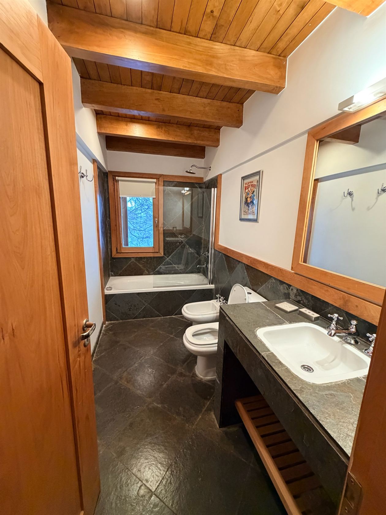 El baño 2 completo: bañera con ducha, bidet y mesada de granito bajo el techo de madera