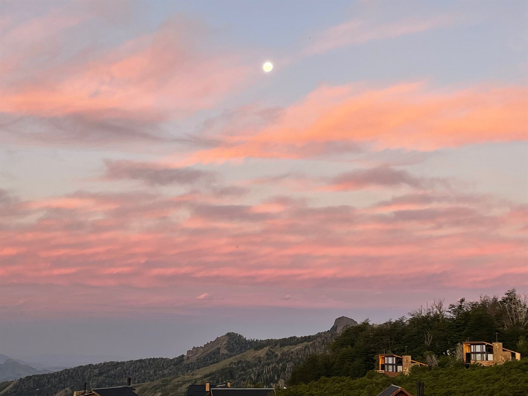 La luna asomando sobre el barrio en un atardecer rosado