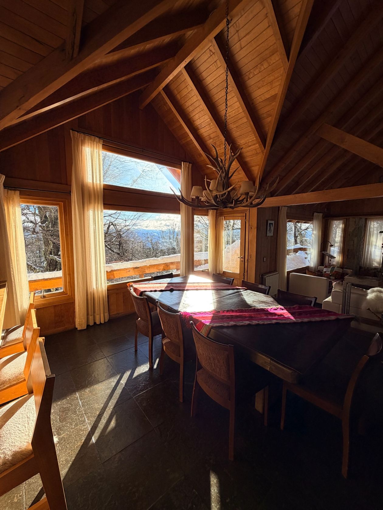 La mesa del comedor para 8 bañada por el sol, con el ventanal al valle nevado