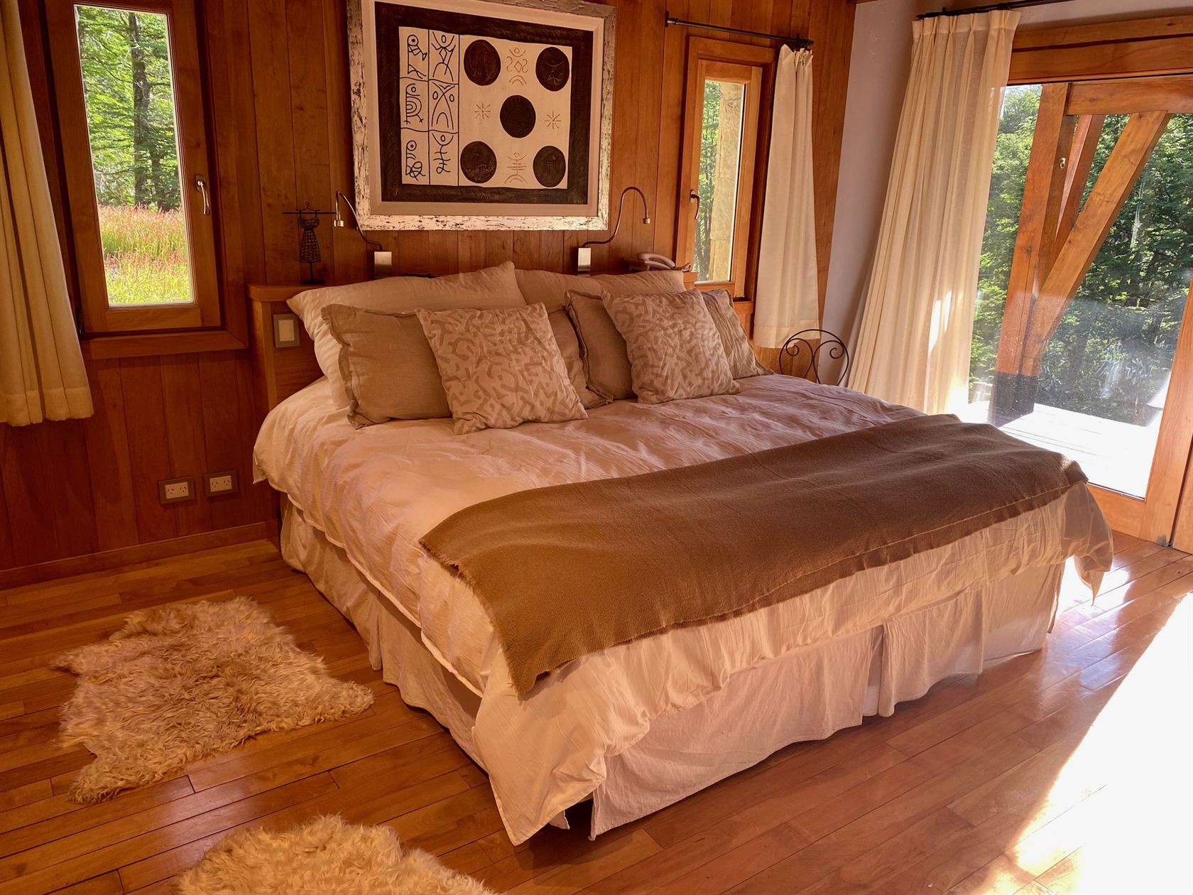 El dormitorio principal con su cama king, el ventanal al deck y el bosque de verano afuera