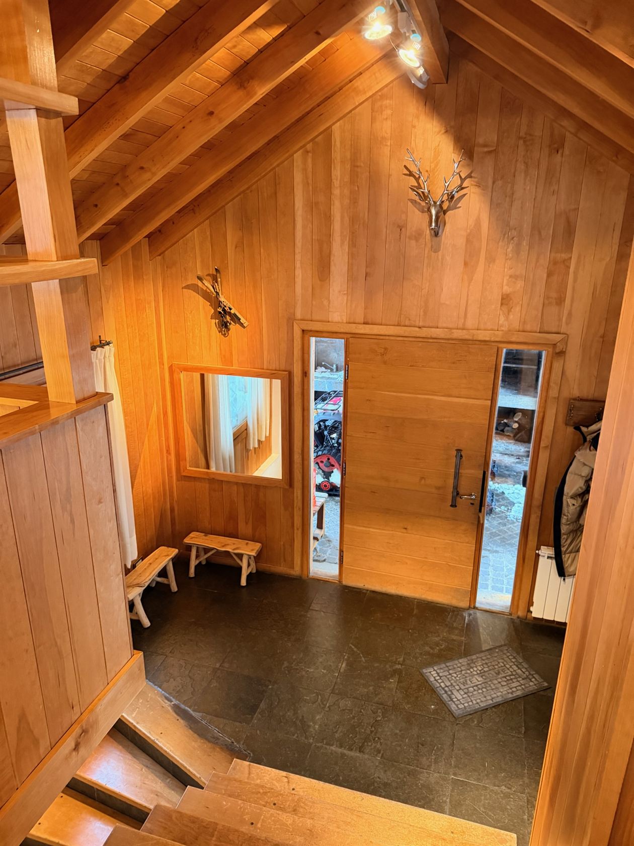 El hall de doble altura y la puerta principal de madera, vistos desde lo alto de la escalera
